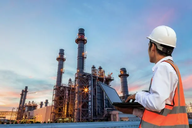 Man working on laptop at oil refinery.